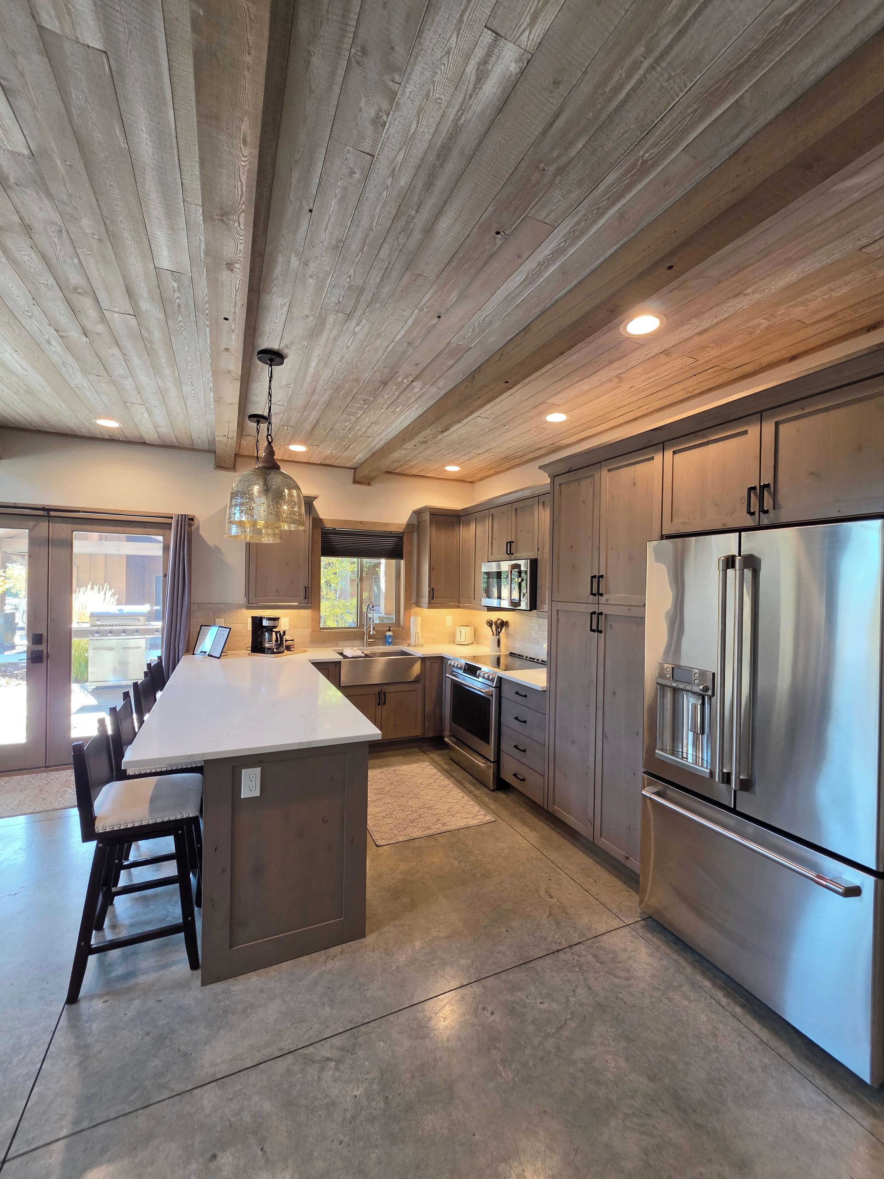 A modern kitchen with a central island, stainless steel appliances, and wooden ceiling beams.