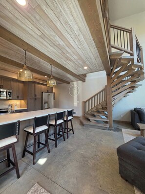 Une cuisine moderne dotée d’un îlot central, de poutres en bois au plafond et d’un escalier avec une rampe en bois.