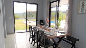 Un coin repas avec une table dressée pour quatre personnes, de grandes fenêtres et une vue sur un paysage verdoyant.