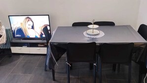 Ein Essbereich mit einem Tisch, Stühlen, einem Fernseher und einem Sessel mit Kissen.