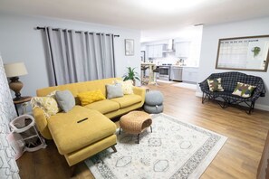 Ein Wohnzimmer mit einem gelben Sofa, einem schwarzen Sessel und einem Teppich mit Muster.