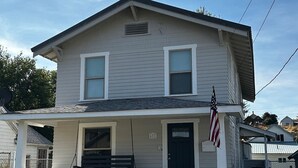 Een huis met twee verdiepingen, een stenen fundering en een veranda, met de Amerikaanse vlag.
