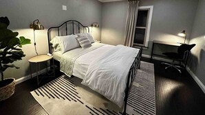 Een moderne slaapkamer met een bed, nachtkastjes, een bureau en een plafondventilator.