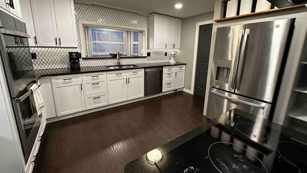 Een moderne keuken met roestvrijstalen apparatuur, witte kasten en een zwart aanrecht.