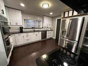 A modern kitchen with stainless steel appliances, white cabinetry, and a black countertop. - Cheerful home with front porch swing. (Pendleton)