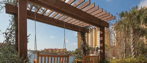 A wooden pergola with swings overlooking a body of water, with buildings in the background.