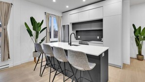 A modern kitchen with a central island, bar stools, and potted plants. - Sunny, bright & natural apt, centrally located (Montréal)