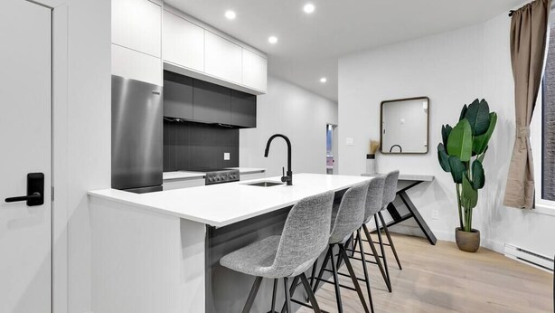 A modern kitchen with white cabinetry, a stainless steel refrigerator, and a bar area with grey barstools. - Spacious & peaceful 2 bedrooms, sleep 6 (Montréal)