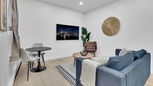 A modern living room with a blue sofa, a round coffee table, and a cityscape painting on the wall. - Spacious & peaceful 2 bedrooms, sleep 6 (Montréal)
