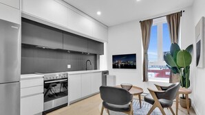 A modern kitchen with white cabinets, a stainless steel stove, and a dining area with two chairs and a small table.