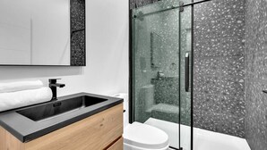 A modern bathroom with a glass-enclosed shower, a white toilet, and a black countertop sink.