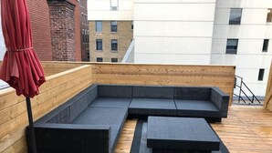 A rooftop seating area with a sectional sofa and a small table, surrounded by wooden deck flooring. - Stunning 2 beds, 2 baths, AAA location, rooftop (Montréal)