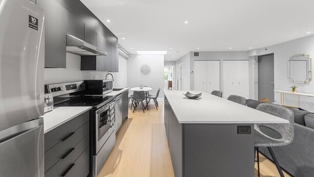 A modern kitchen with a central island, built-in appliances, and a dining area with a round table and chairs. - Stunning 2 beds, 2 baths, AAA location, rooftop (Montréal)