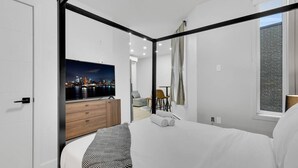 A modern hotel room with a large bed, a flat-screen TV, a wooden dresser, and a city view. - Lovely, spacious & stylish studio, sleeps 3 (Montréal)