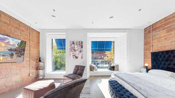 Une chambre moderne dotée d ’un grand lit, d’un coin salon avec un fauteuil et un pouf, et offrant une vue sur l’extérieur grâce à de grandes fenêtres.
