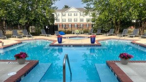 A rectangular swimming pool with a metal ladder, surrounded by a brick border and potted plants.