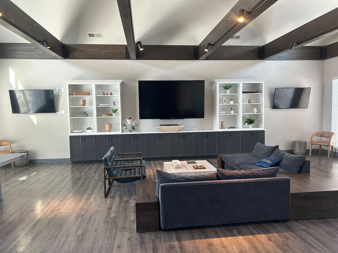 A modern living room with a large flat-screen TV, grey sofas, a coffee table, and built-in shelving with decorative items.