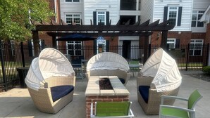 An outdoor seating area with a brick table and wicker chairs, some covered with white canopies, and a metal chair in the foreground.