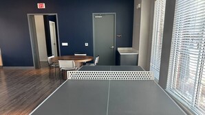 A ping pong table with a 'Cornilleau' logo, a door, a window with blinds, and a chair.