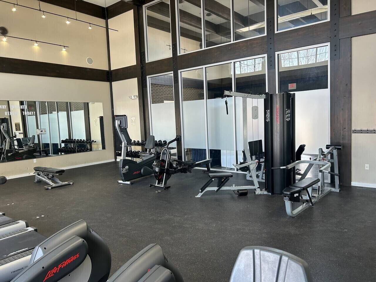 Une salle de sport équipée de divers appareils d’exercice, dotée de grandes fenêtres et d’un mur entièrement recouvert de miroirs.
