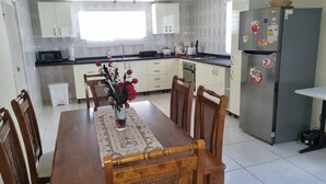 Een moderne keuken met witte kastjes, een eettafel met stoelen, een koelkast en een magnetron.