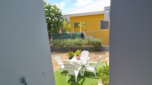 Uitzicht vanaf een balkon op een patio met een tafel en stoelen, omgeven door groen en een geel gebouw.