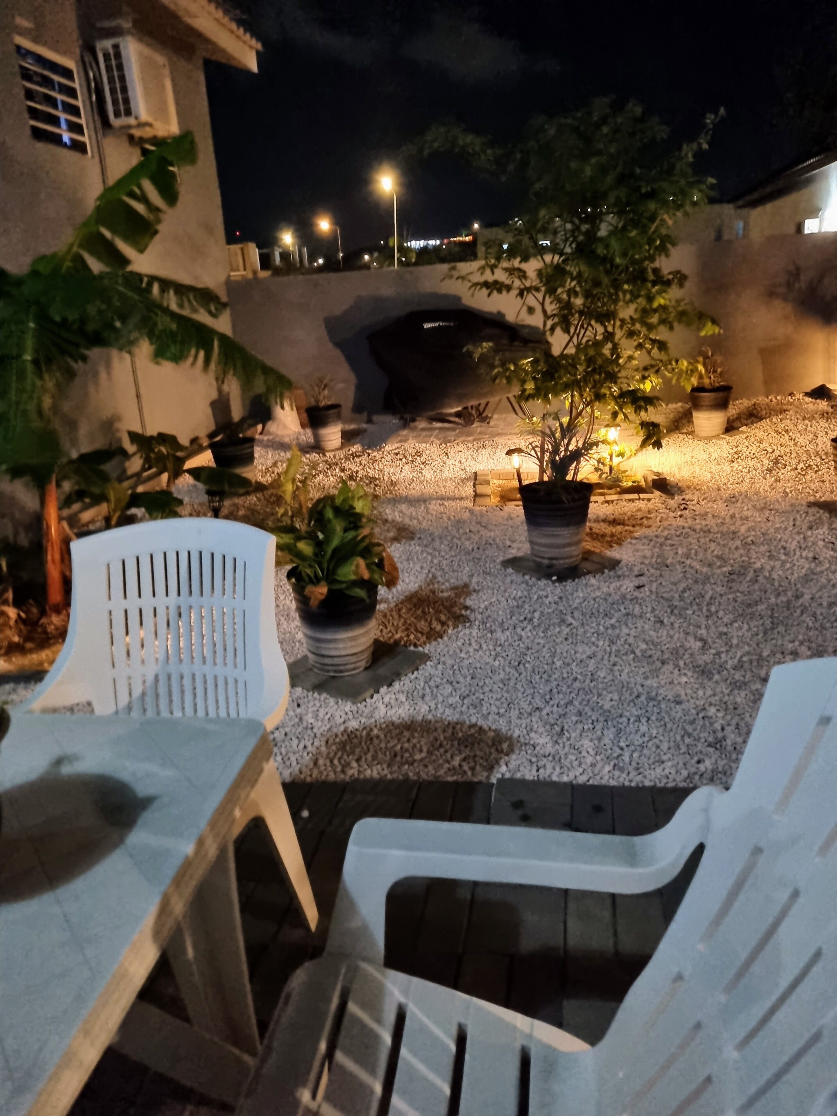 Un patio con mobiliario exterior, plantas en macetas y una parrilla.