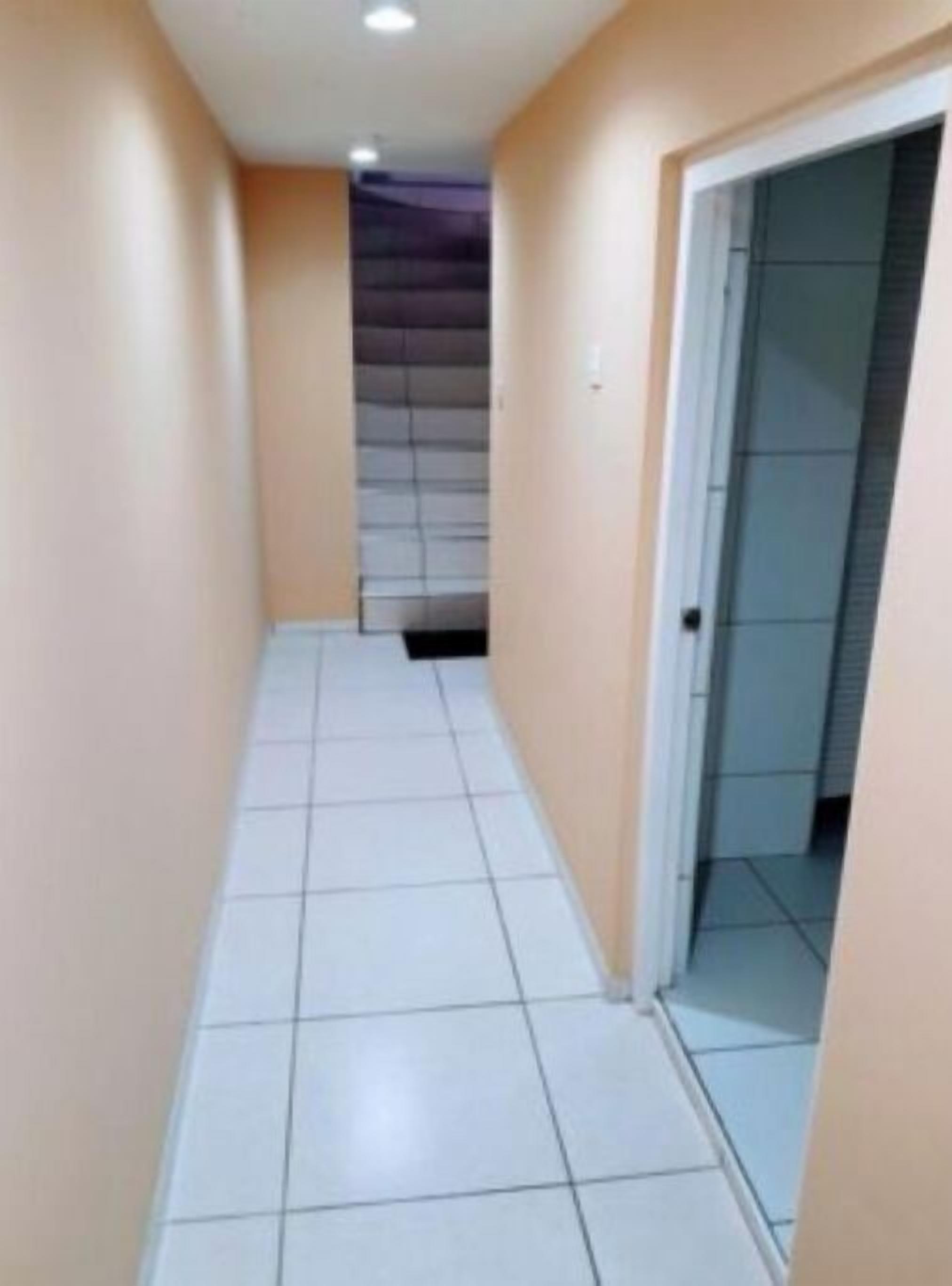A narrow hallway with white tiled flooring and beige walls.