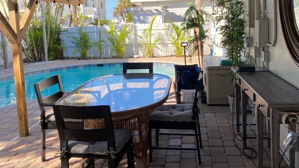 Patio esterno con tavolo e sedie rotonde, piscina e area coperta con ventilatore a soffitto.