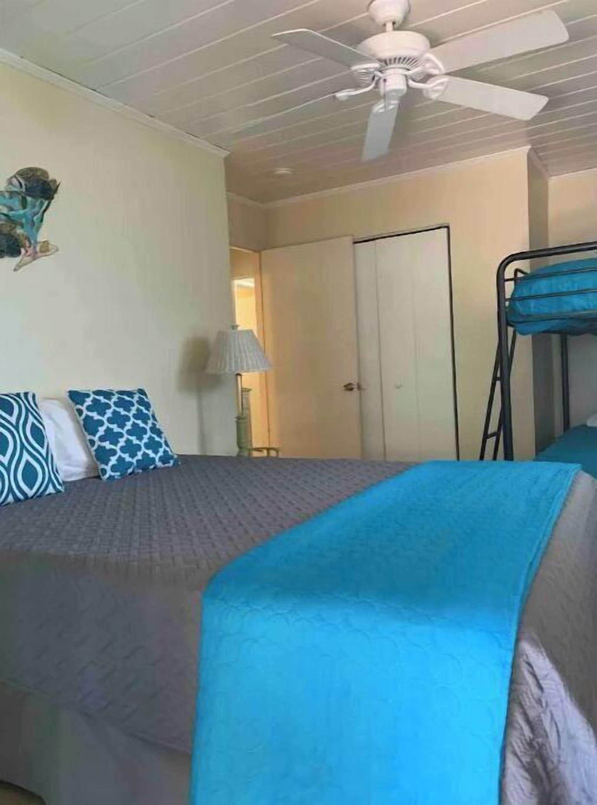 A bedroom with a bed, a ceiling fan, a door, and a bunk bed.