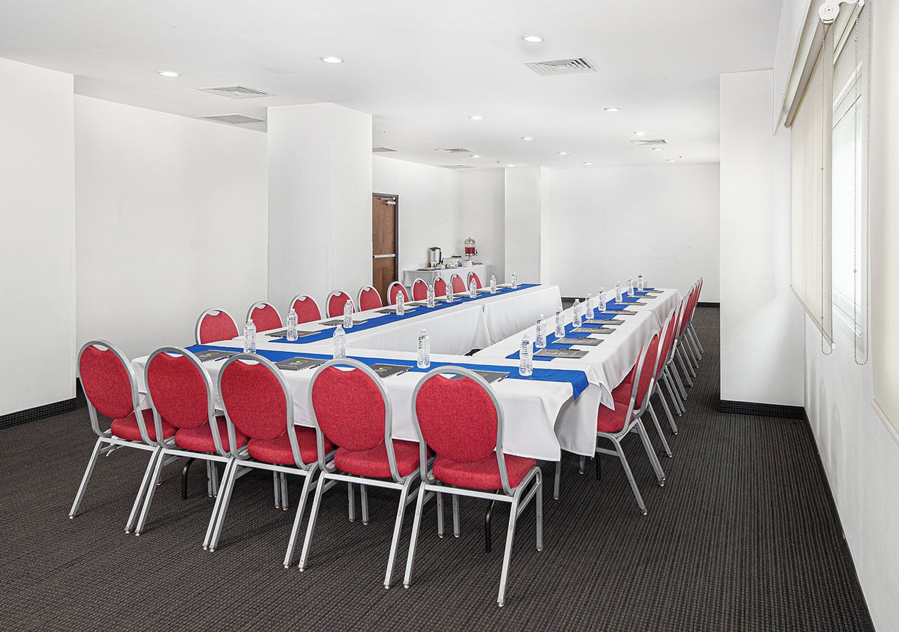 A conference room with a long table, red chairs, and white tablecloths.