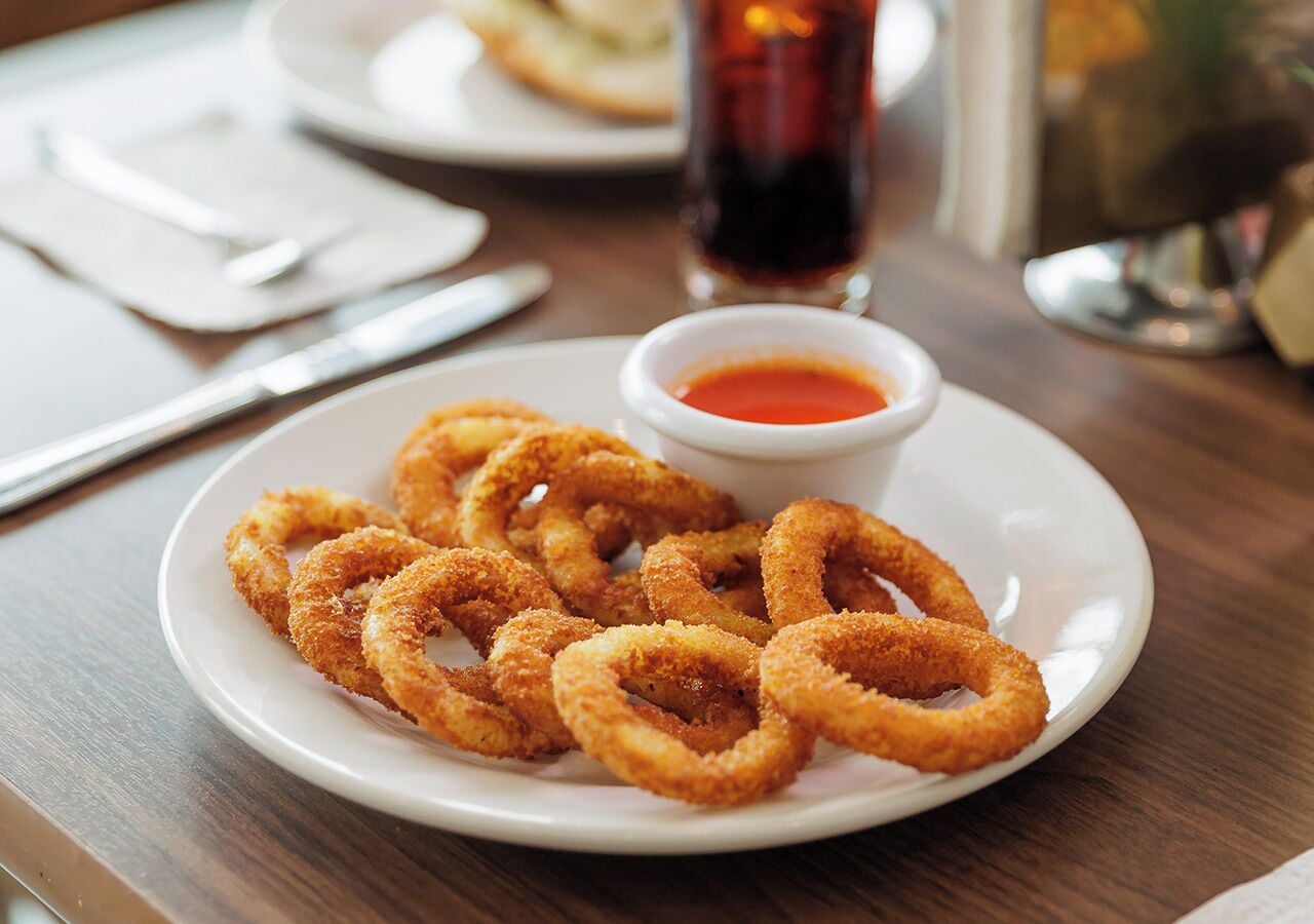 Une assiette d'anneaux d'oignon frits, accompagnés d'une sauce pour tremper, sur une table en bois.