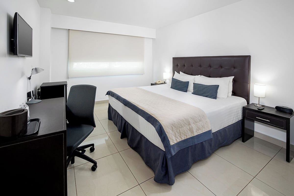 Una habitación de hotel moderna con una cama grande, un escritorio, una silla y un televisor montado en la pared.