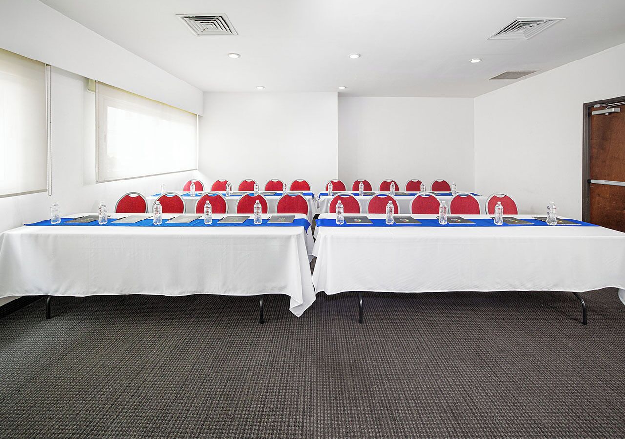 A conference room with two long tables, each with red chairs and water bottles.