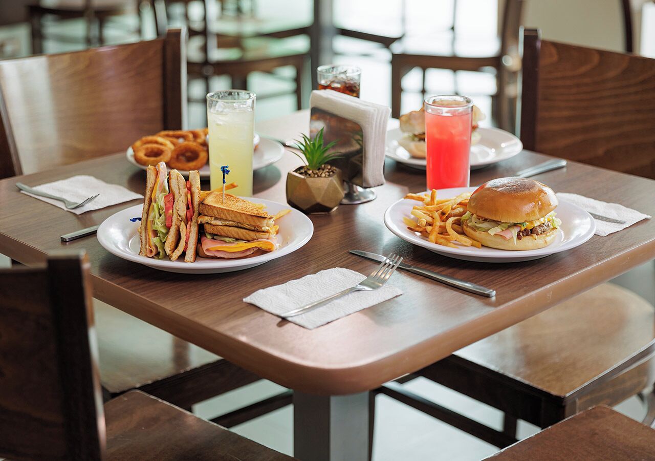 A dining table with plates of food, including sandwiches and fries, and two drinks.