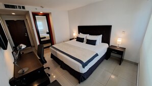 Habitación de hotel con una cama grande, mesitas de noche, un escritorio con silla, una lámpara de escritorio y un espejo.