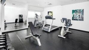 Un gimnasio con equipo de ejercicio, un espejo y carteles motivacionales en las paredes.