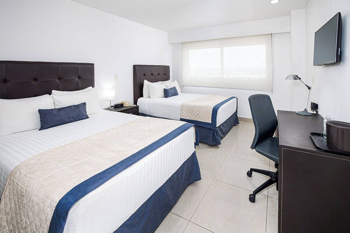 Habitación de hotel con dos camas, un escritorio, una silla, un televisor y una ventana.