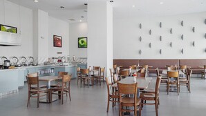 Un comedor amplio con varias mesas y sillas, una zona de cocina con electrodomésticos modernos, y una pared con lámparas decorativas.