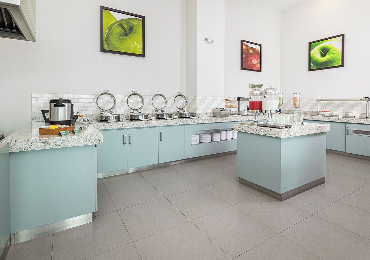 A modern kitchen with light blue cabinets, granite countertops, and stainless steel appliances. There are three round mirrors on the wall, and the floor is tiled.