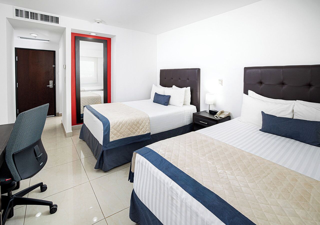 A hotel room with three beds, a desk, and a chair.