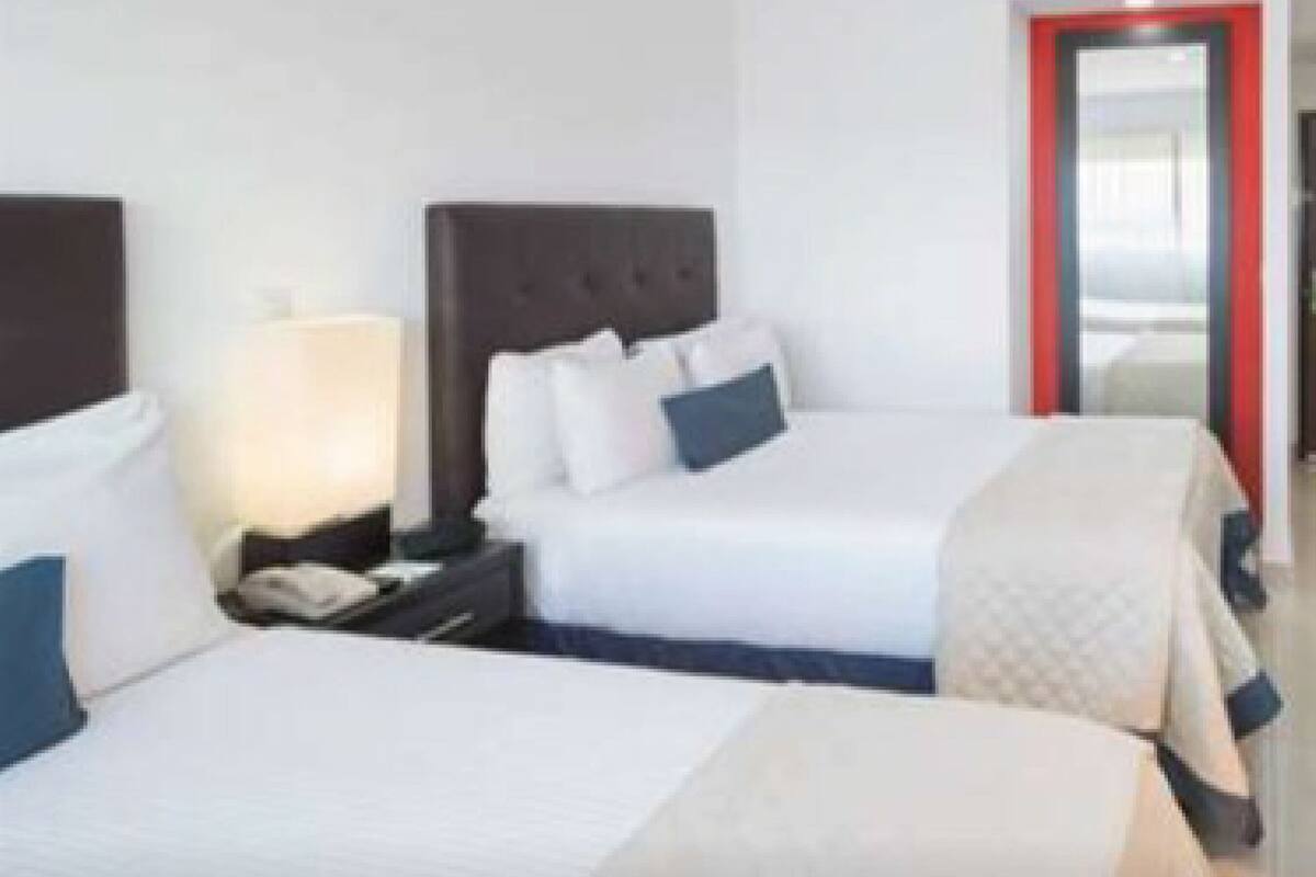 Una habitación de hotel con dos camas, una mesita de noche con lámpara y una puerta con marco rojo.