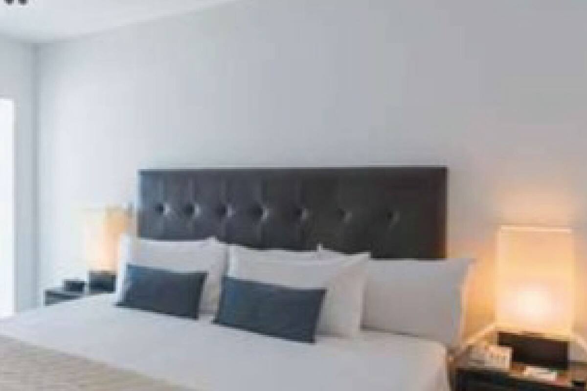 Una habitación de hotel con una cama grande, un cabecero oscuro, dos mesitas de noche con lámparas y una ventana.