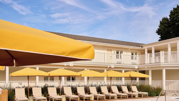 A poolside area with lounge chairs and yellow umbrellas. - Oyster Estate (Greenport)
