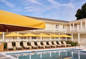 Zona junto a la piscina con sillones de descanso y sombrillas amarillas.