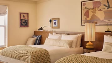 A hotel room with two beds, a large window, a ceiling fan, and a painting on the wall.
