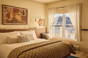 Un dormitorio con una cama grande, una ventana con cortinas, una lámpara de pared y una obra de arte enmarcada.