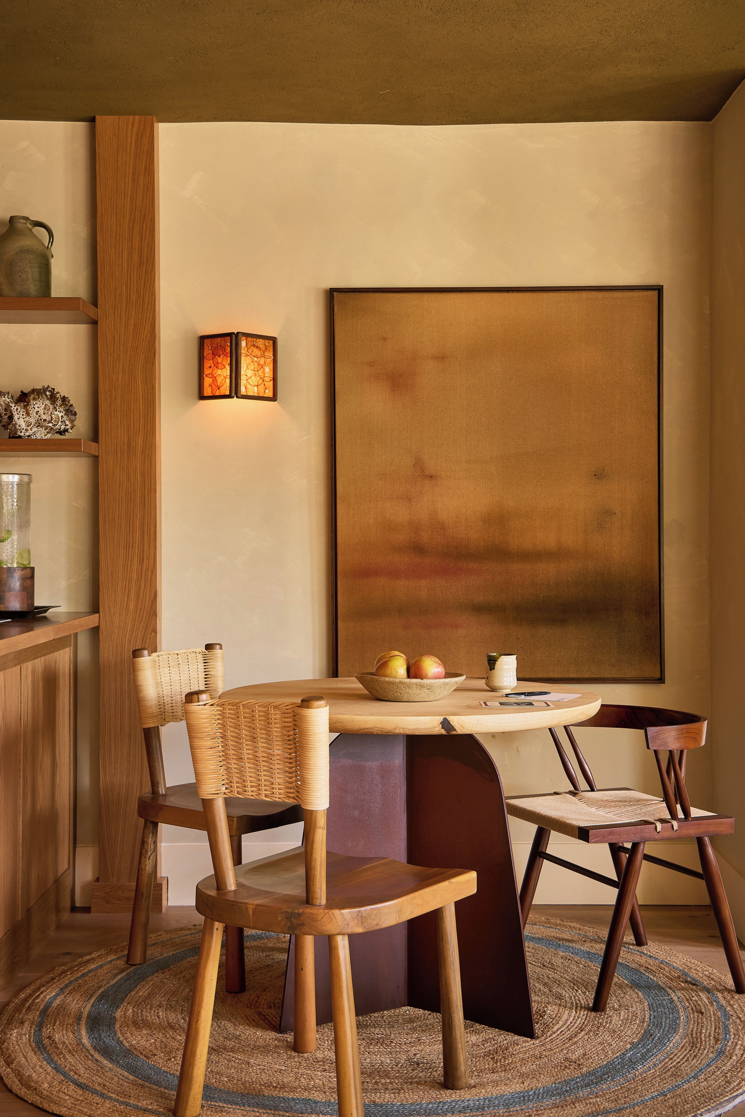 A dining area with a round table, chairs, a vase, and a painting on the wall.