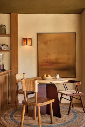 Un comedor con una mesa redonda, sillas, un jarrón y un cuadro en la pared.