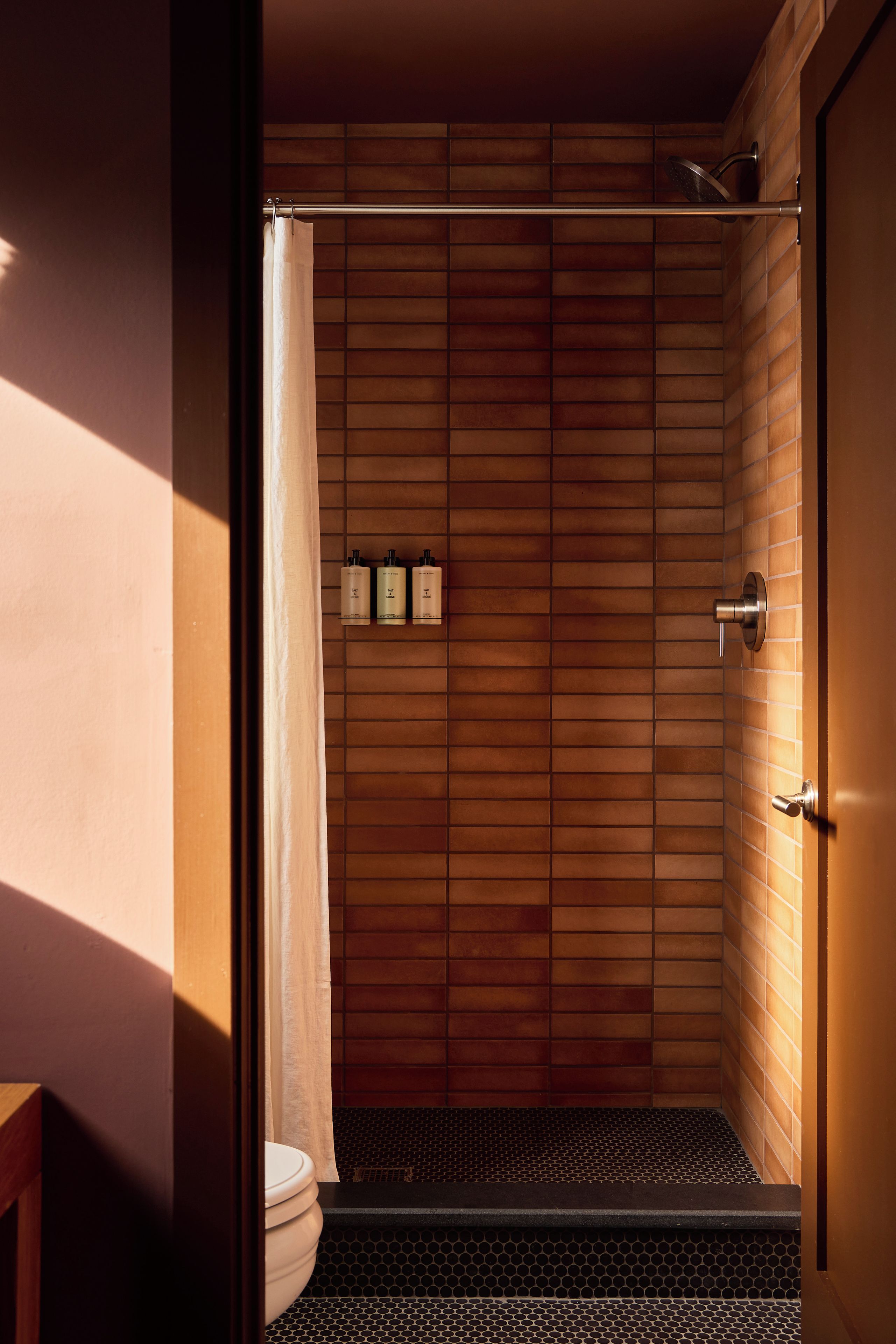 Cabina de ducha de madera con pared de azulejos, un cabezal de ducha y un inodoro visible a través de la puerta.